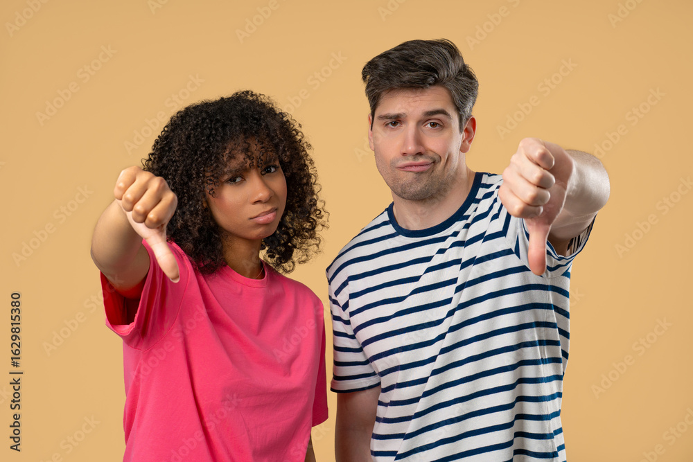 Interracial Couple Giving Thumbs Down Dislike With Disapproving Look On Beige Interracial Couple Giving Thumbs Down Dislike With Disapproving Look On Beige