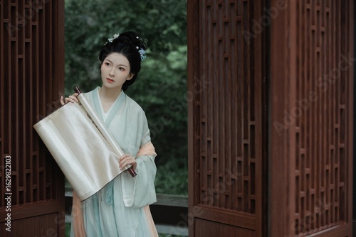 Elegant young woman in traditional clothing holding scroll.