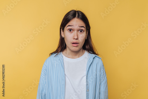 Obraz na płótnie portrait of young startled girl reveals a shocked expression on yellow backgroun