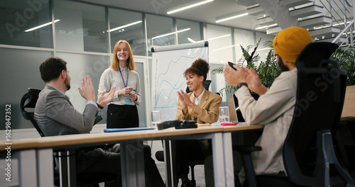 Woman stands at whiteboard while colleagues sit at table