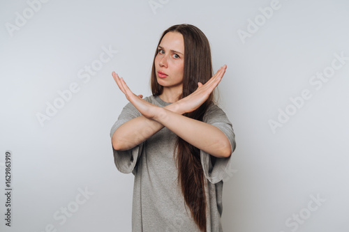 portrait of young woman expresses disapproval by crossing her arms in a negative manner like showing stop sign on light background