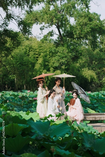 Four women in traditional dress with umbrellas in a lotus field.