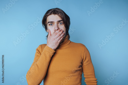 Fotografia portrait of young man covers his mouth with his hand, expressing shock or disbel