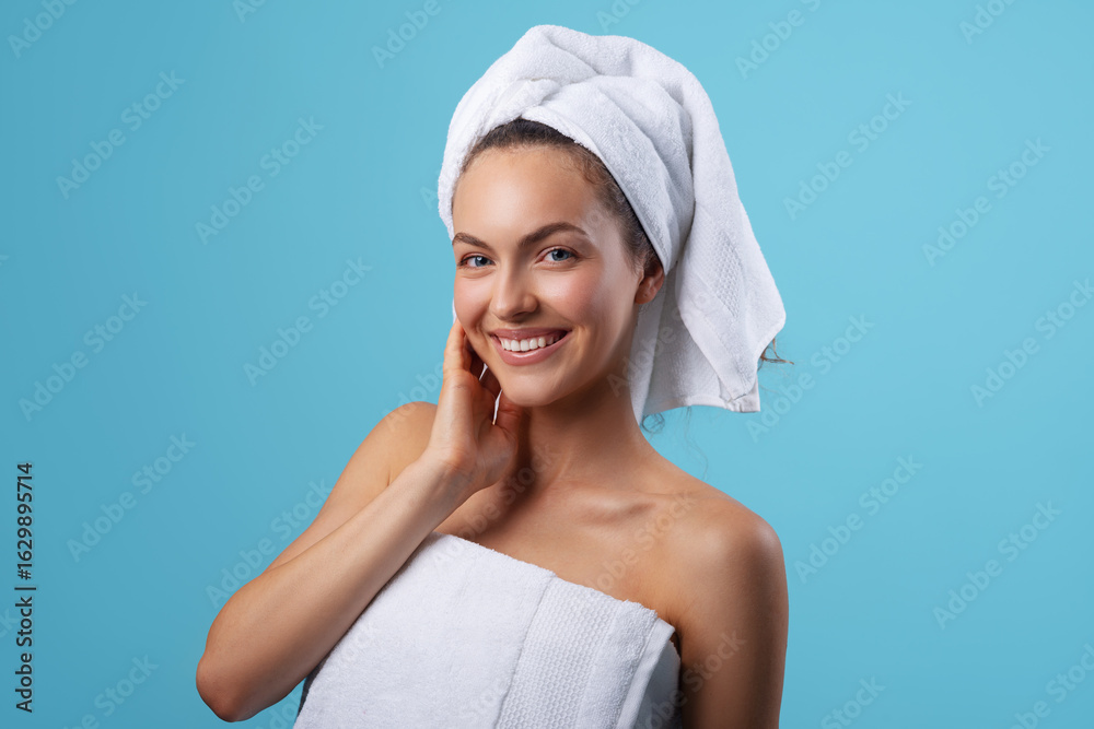 Smiling beautiful young woman, wrapped in a white towel, standing against a blue background Smiling beautiful young woman, wrapped in a white towel, standing against a blue background