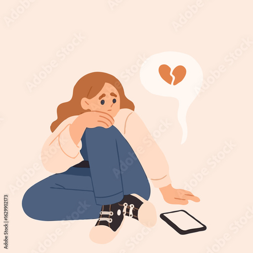 Young woman sitting on floor looking sad at phone with heartbroken icon  