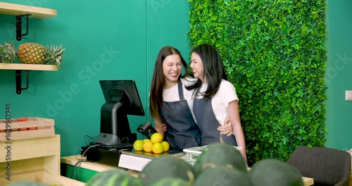 Asian LGBTQ partner standing beside smiling Caucasian co-owner preparing fruit counter together at tropical grocery shop before store opens in morning