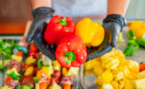 Chef hands in black gloves holding fresh red and yellow bell peppers ready for cooking. Colorful vegetables prepared for healthy meal, grilling, or salad concept