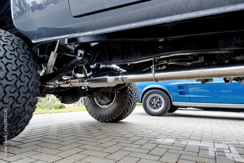 Papier peint Close-up view of a custom side exhaust pipe and suspension on a lifted off-road vehicle parked on a brick pavement with a parking sign for people with limited mobility