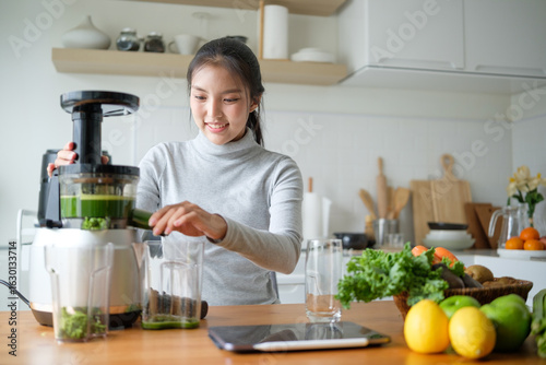 Cuadro en lienzo Smiling young woman preparing a healthy green juice using a slow juicer in a bright kitchen