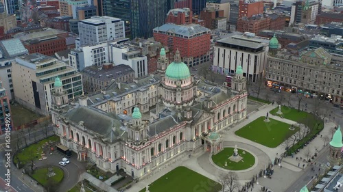 Wide-angle aerial orbit of Belfast City Hall during a peaceful evening, capturing the building’s illuminated façade and calm city atmosphere.