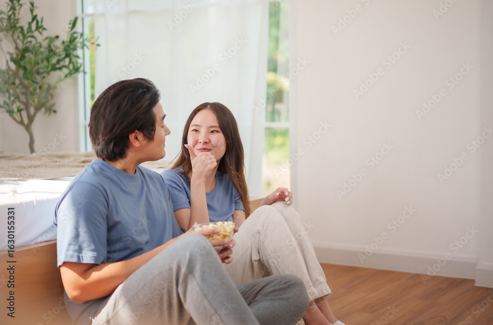 Young Asian man and woman sharing popcorn on floor, smiling and bonding during snack time Young Asian man and woman sharing popcorn on floor, smiling and bonding during snack time