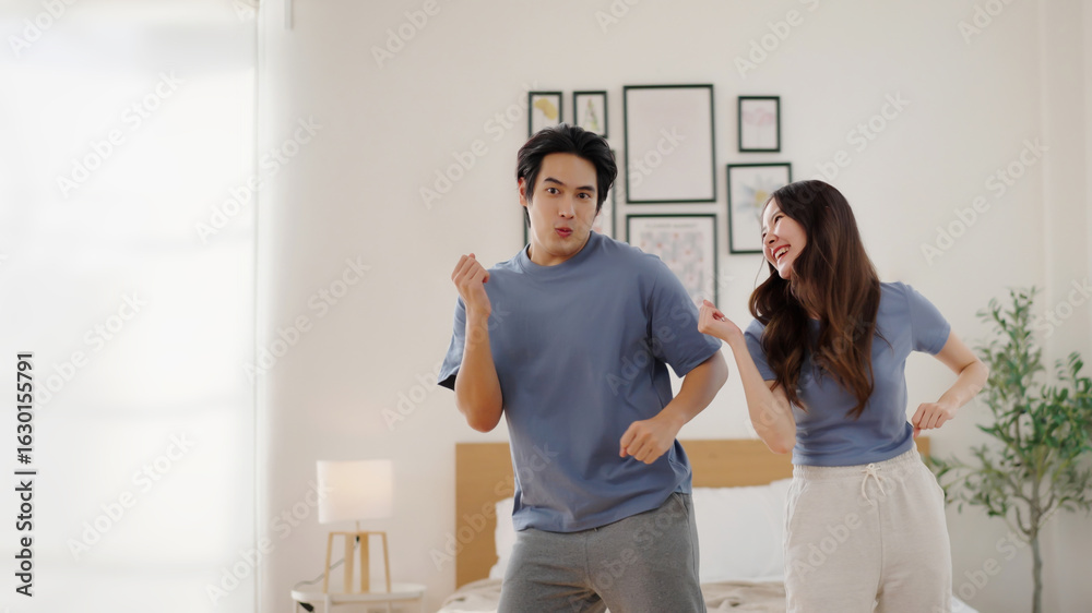 Fototapeta premium Happy Asian man and woman enjoying a fun moment dancing together at home in casual clothes