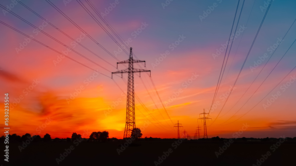 Fototapeta premium Summer sunset or sundowner view with a dramatic sky and overland high voltage lines near Tabertshausen, Aholming, Deggendorf, Bavaria, Germany