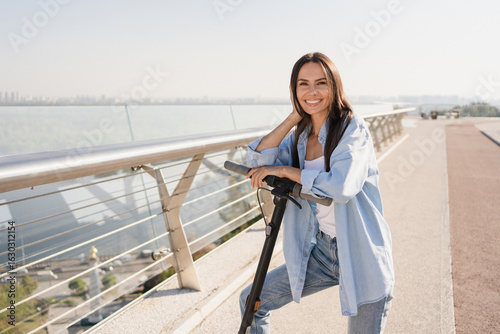 Fototapet Smiling woman using mobile app for electric scooter rental while has excursion traveling exploring riding in the city center