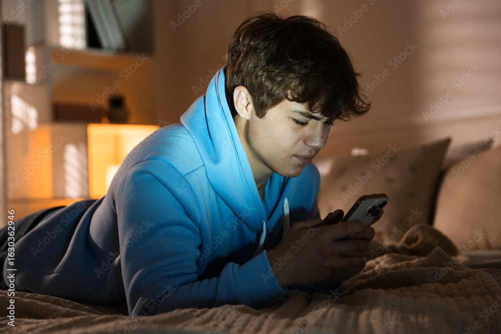 Fototapeta premium Teenage boy using smartphone on bed at home