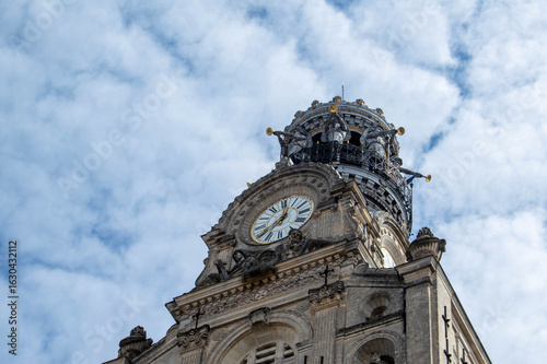 French ecclesiastical heritage: Low angle view of the belfry and clock tower of Église Sainte-Croix under a cloudy sky in Nantes, France.
