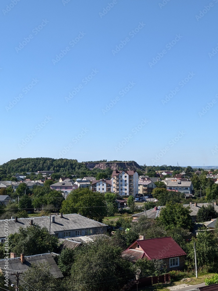 Obraz premium Panoranmic view of a small town with residential areas and green hills in the background. Daytime urban scene. 