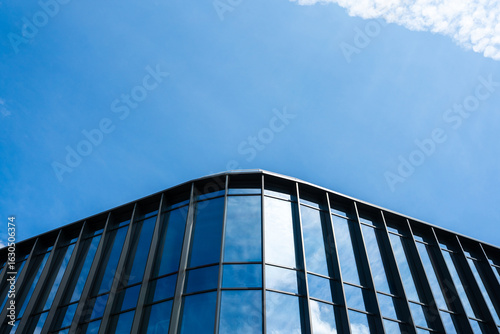 Contemporary glass facade with vertical metal frames reflects the clear blue sky and clouds. Suitable for illustrating architecture, business, or urban development concepts.