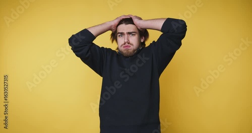 young man expresses frustration by holding his head, capturing a relatable moment of stress on yellow background