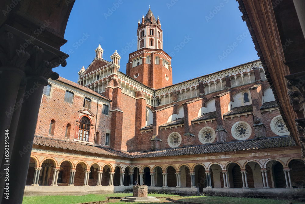 Fototapeta premium Vercelli, Italy: The historic cloister of the Basilica di Sant'Andrea, with its Romanesque and Gothic architecture, framed by a bell tower against a blue sky.