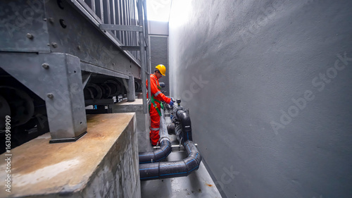 Worker inspecting industrial pipes in narrow alley during daylight hours