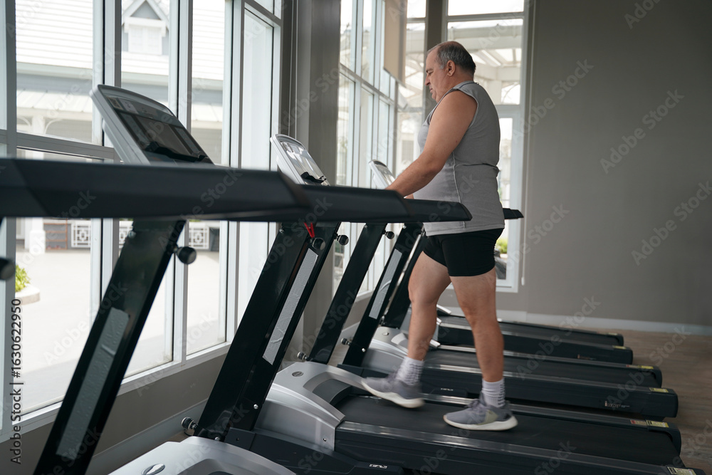 Fototapeta premium Man exercising on treadmill in bright fitness center during daytime