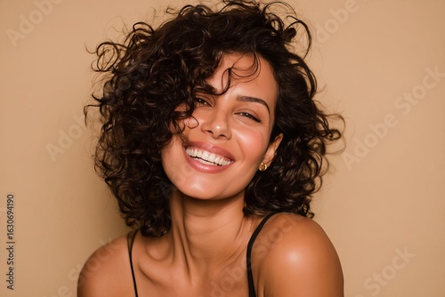 A vibrant woman with curly hair flashes a warm smile against a neutral background radiating happiness and positivity