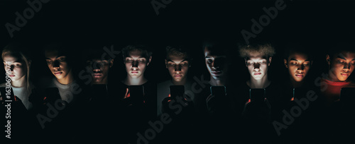 Teenagers staring at smartphones in darkness with screen glow. Social media addiction and digital dependence among youth