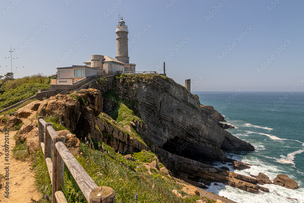 Obraz premium Santander, Spain. Sunny day view of Cabo Mayor Lighthouse perched on cliffs above the Bay of Biscay, with rocky coast and sea surrounding the ash-stone cylindrical tower