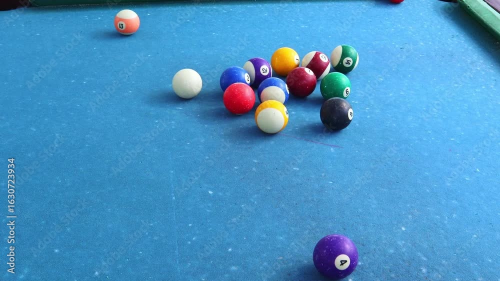 A close-up view of a billiard table with colorful balls arranged in a triangle. The balls spill to the sides from the impact The blue felt surface contrasts with the vibrant colors of the balls.