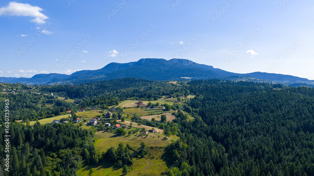 Obraz premium Drone photo of a wide forested Romanija mountain with rocky ridges and rural clearings under a bright blue sky