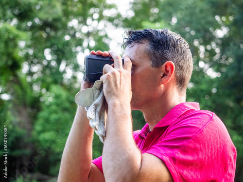 Photos White male looking through rangefinder on golf course.
