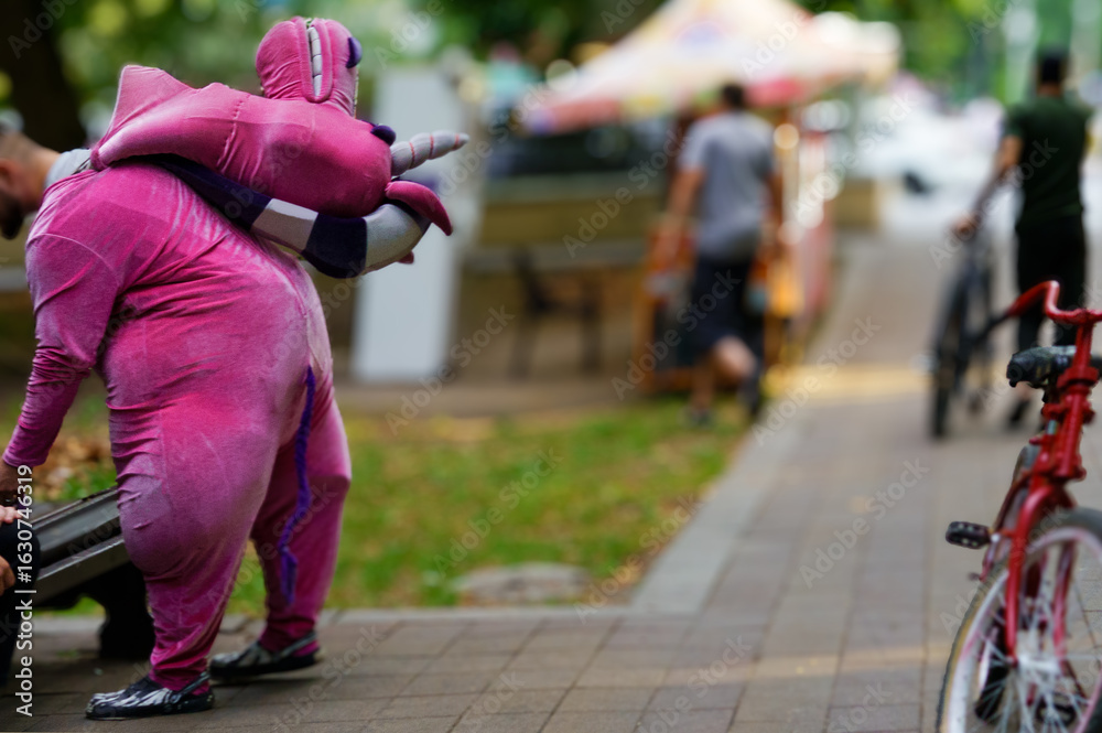 Naklejka premium Person in a colorful costume interacts with park visitors during a sunny afternoon in a vibrant urban setting