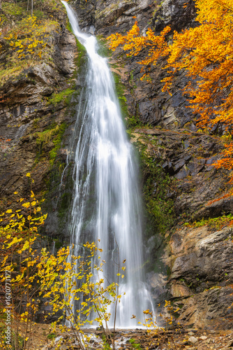 The Sutovsky waterfall in The Mala Fatra national park in Slovakia, Europe. Autumnal Waterfall: Water cascades down rocky cliff, framed by vibrant fall foliage in a scenic nature setting.