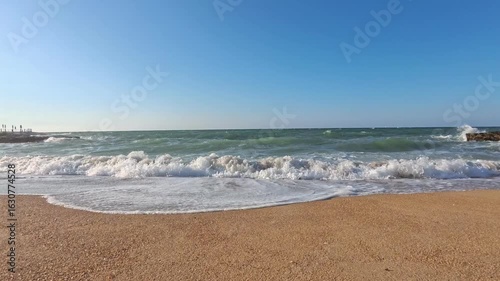 Waves Gently Washing the Sandy Beach with Rocks under a Clear Blue Sky – Peaceful Ocean Shoreline at Sunset. Italy, Puglia, Torre a Mare