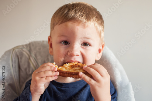 Obraz na plátně A fair-skinned boy with blonde hair is eating a grilled cheese sandwich