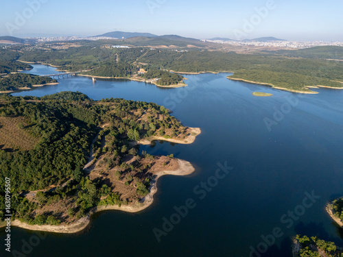Aerial view of Ömerli Dam with vivid blue waters, lush green forests, and curving shorelines under a clear sky, capturing the peaceful and untouched beauty of Istanbul’s largest reservoir.

