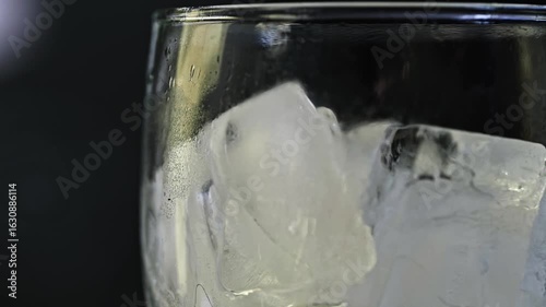 Green Soda Beverage Poured in Glass with Ice Cubes.  Glass rotating in slow motion. Soft Lighting on Dark Background
