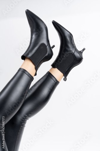 Un par de elegantes botines negros de tacón de gatito y leggings brillantes sobre fondo blanco