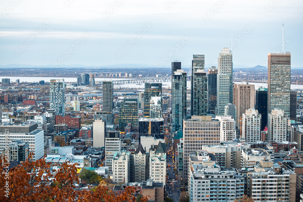 Fototapeta premium Wide panorama from Mount Royal overlooks downtown Montreal, Quebec, where glass and steel skyscrapers rise beside the St Lawrence River and the Jacques Cartier Bridge, illustrating Canada economy.