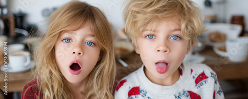 Two siblings with blonde hair and blue eyes mimicking yelling with playful expressions indoors