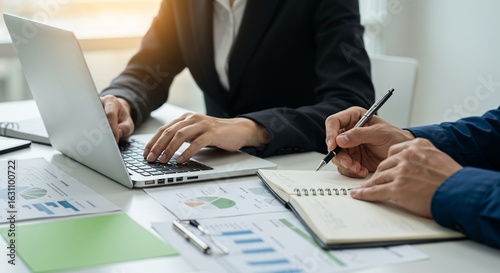 Business professionals in a collaborative meeting, analyzing financial charts and data on a laptop and notebook.