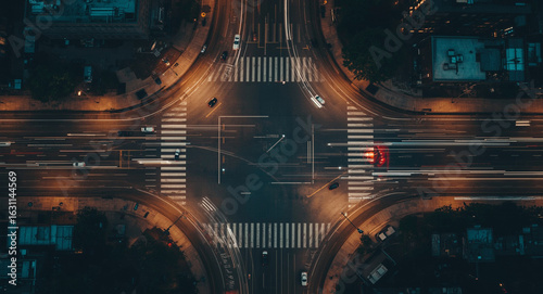 An aerial top-down view of a city street intersection at night with long exposure light trails from moving cars.