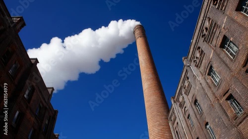 Low angle shot of a tall brick smokestack against a clear blue sky backdrop