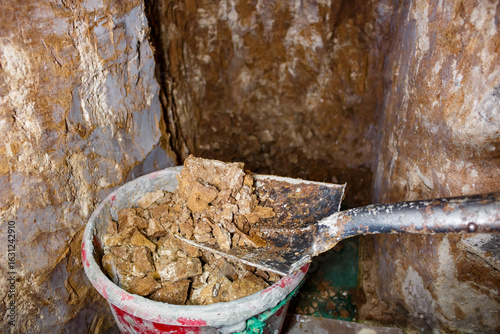 Putting soil into a bucket while manually digging a tunnel with a shovel
