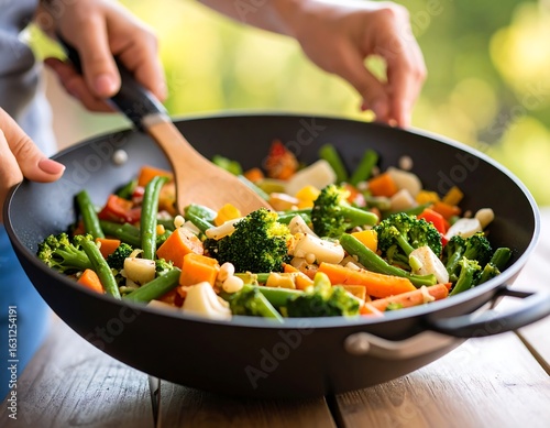 A person stirs colorful mixed vegetables in a wok outdoors