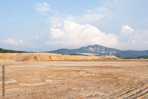 Expansive construction site with exposed earth and heavy machinery tracks. Surrounded by distant mountains, the scene captures early stages of land development and earthmoving operations.