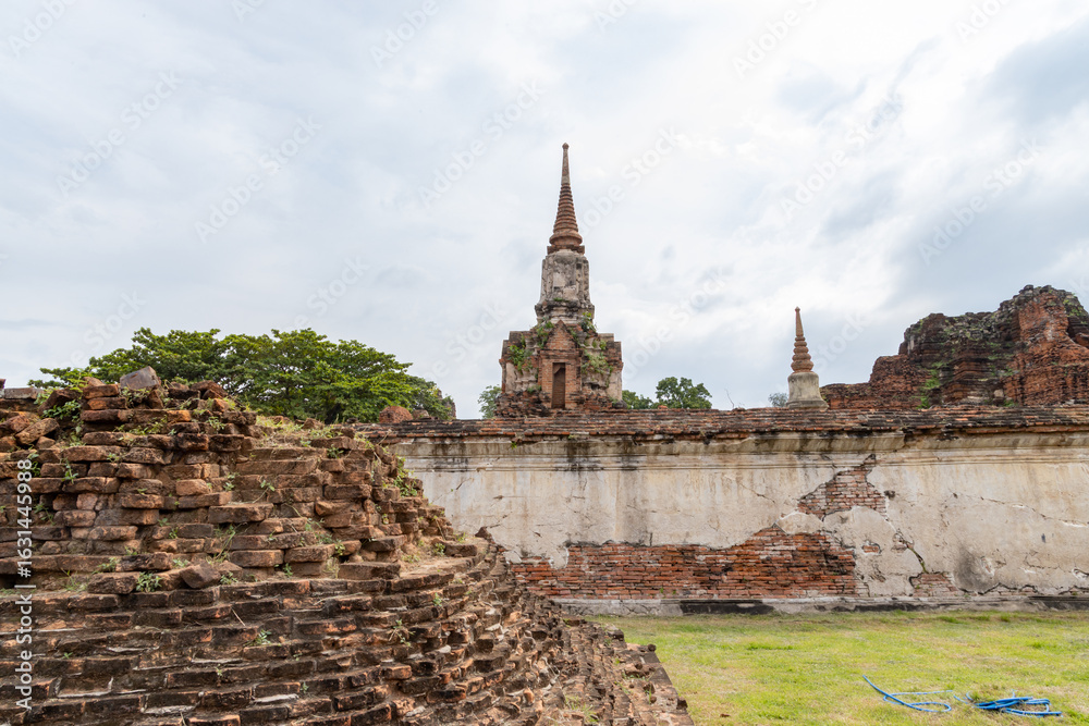 Fototapeta premium Ancient stupa and temple ruins behind a weathered brick wall at Wat Phra Ram in Ayutthaya, Thailand
