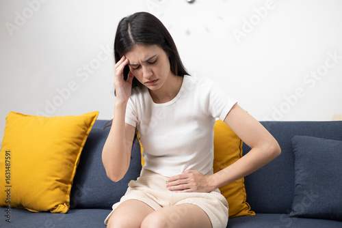 Foto Young woman suffering from abdominal pain and menstrual cramps, lying and sitting on the sofa at home, having cramps in the abdomen, female health concept