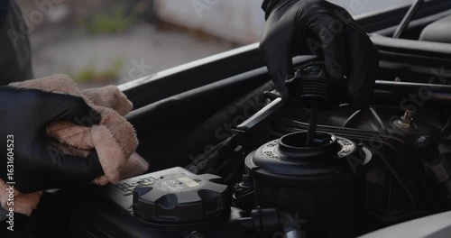  Male hands in gloves check the oil level with a dipstick in a car. Taking care of the engine compartment